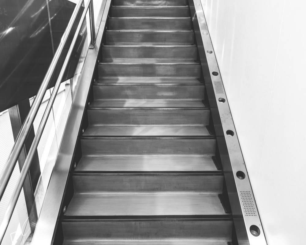 内観（モノトーン）。階段の左側にステンレスの手すり、右側の足元には照明とスピーカーが埋め込まれている。