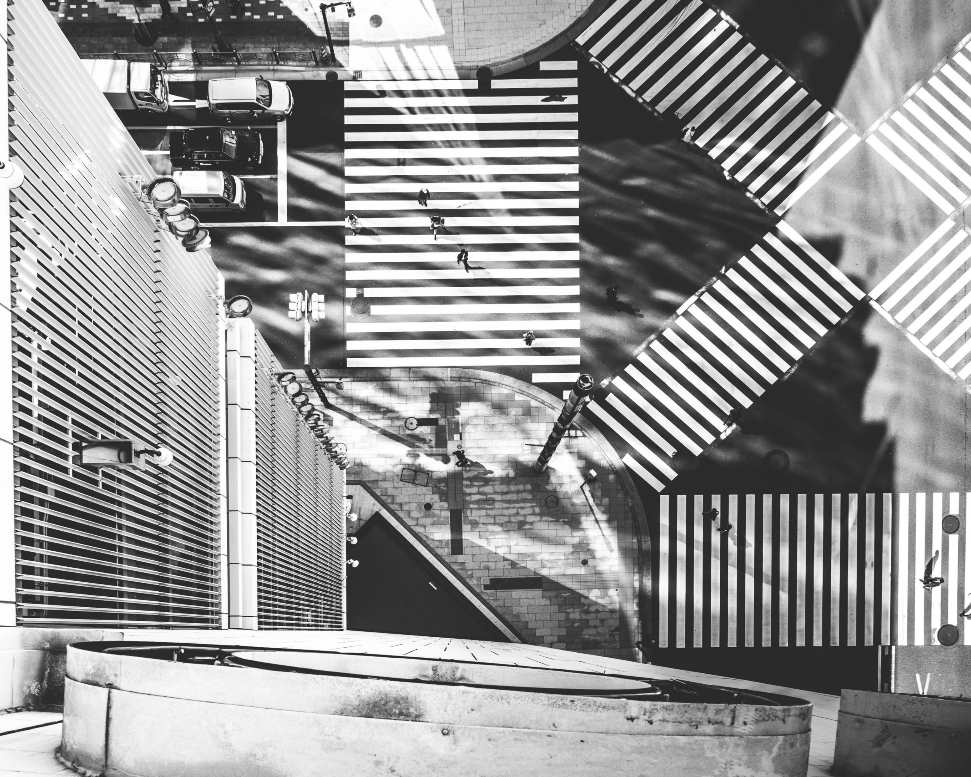 外観（モノトーン）。屋上からのネオンサイン越しの俯瞰で、交差点や歩道、角地の三角形の広場的なスペースがある。