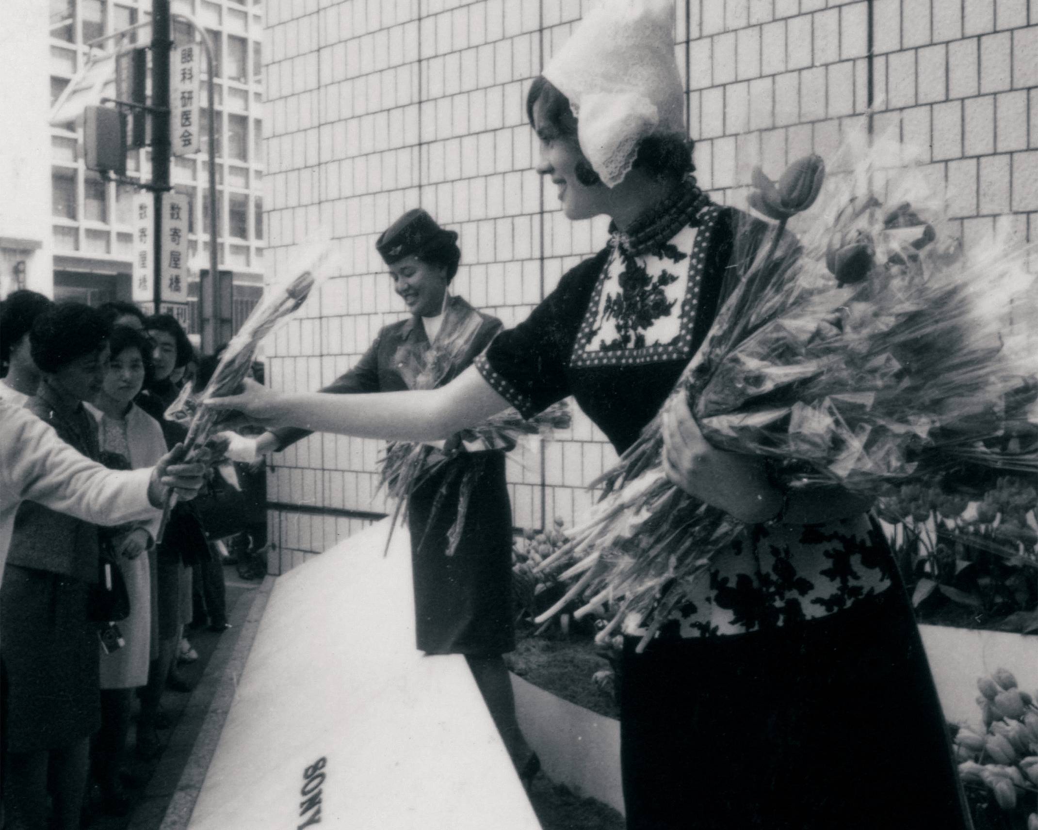 イベントの様子（モノトーン）。ソニースクエア（屋外イベントスペース）でオランダの民族衣装を着た女性と客室乗務員がチューリップを配布している。