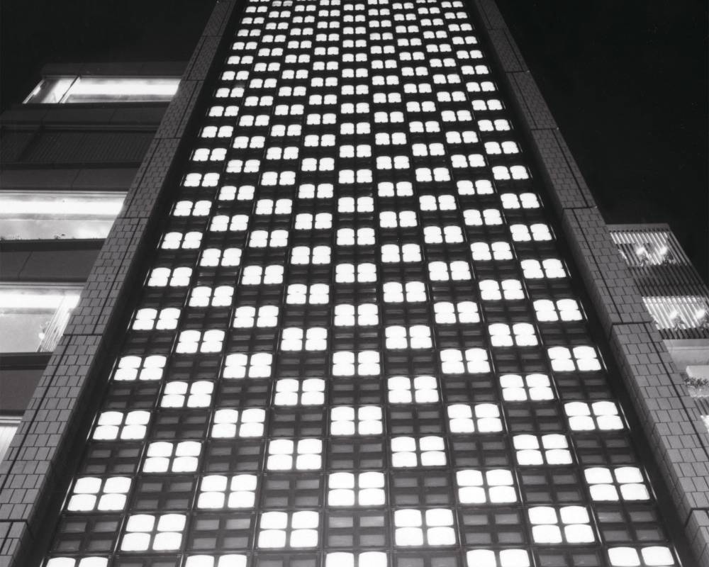 外観（モノトーン）。晴海通り側の壁面に隙間なく埋め込まれたブラウン管テレビの点灯と消灯で市松模様を作り出している。