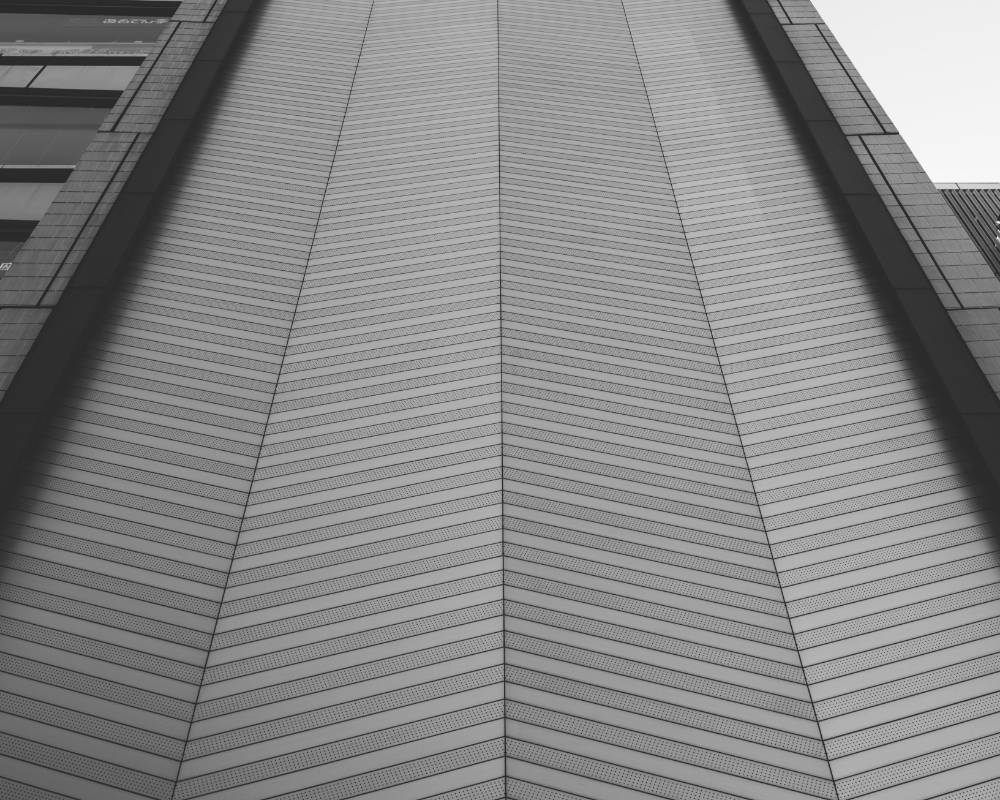 外観（モノトーン）。晴海通り側の外壁は、ヘアライン加工のアルミスパンドレルがヘリンボーン模様に並んでいる。