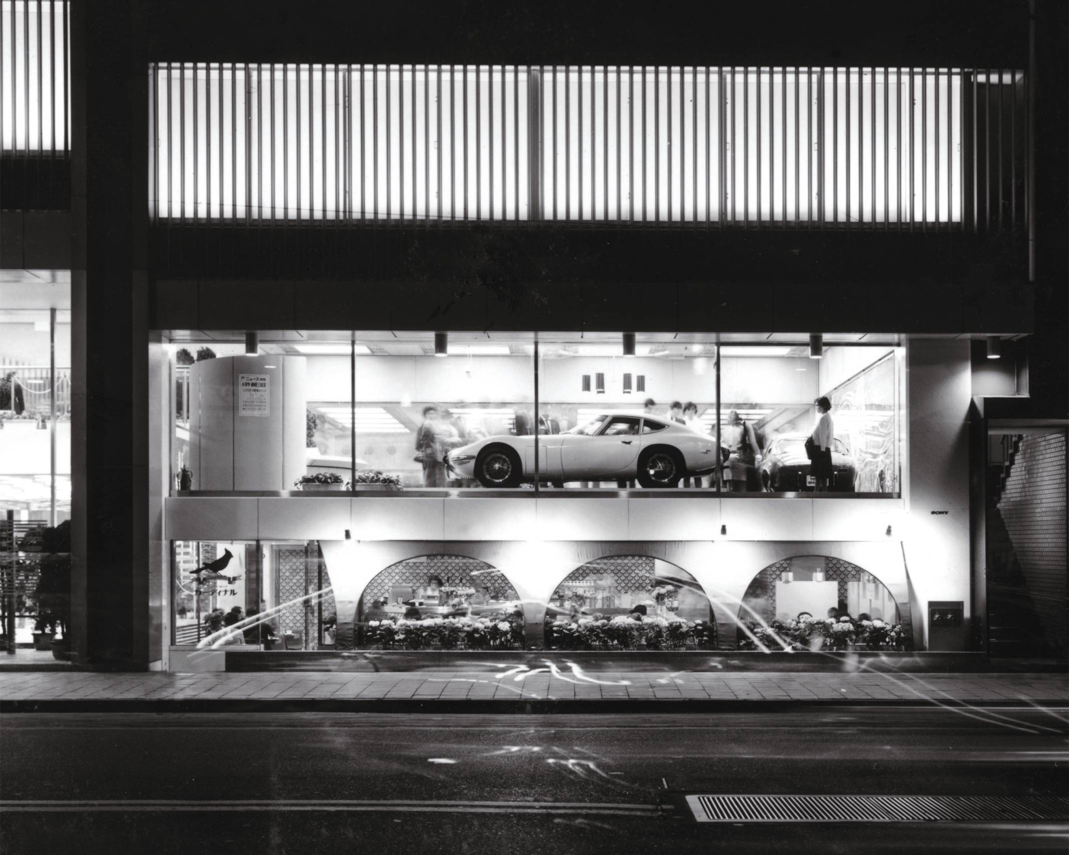 外観（モノトーン）。外堀通り側1階にはコーヒーショップがあり、2階にはウインドー沿いに車がディスプレイされている。