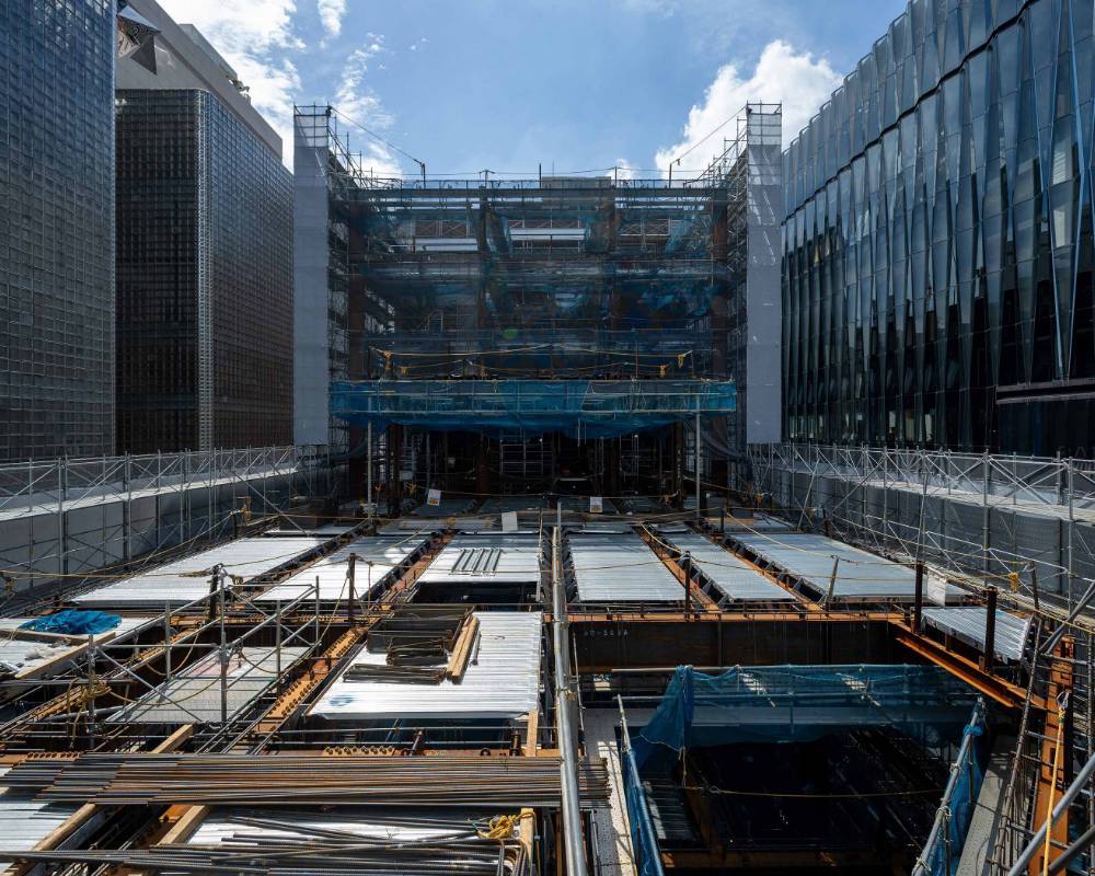 外観。コンクリート打設前の足場に囲われた屋上階の躯体工事。床面には鉄骨とデッキが露わになっている。