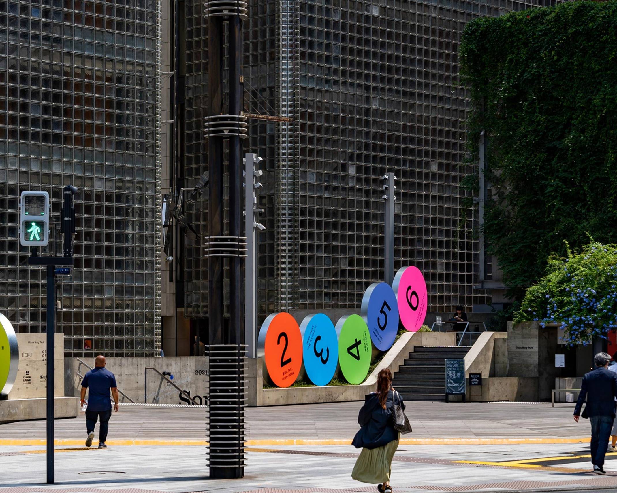 外観。地上階に1から6までの数字それぞれ描かれた6つの丸いオブジェが並んでいる。隣接した歩道を歩く人々がいる。
