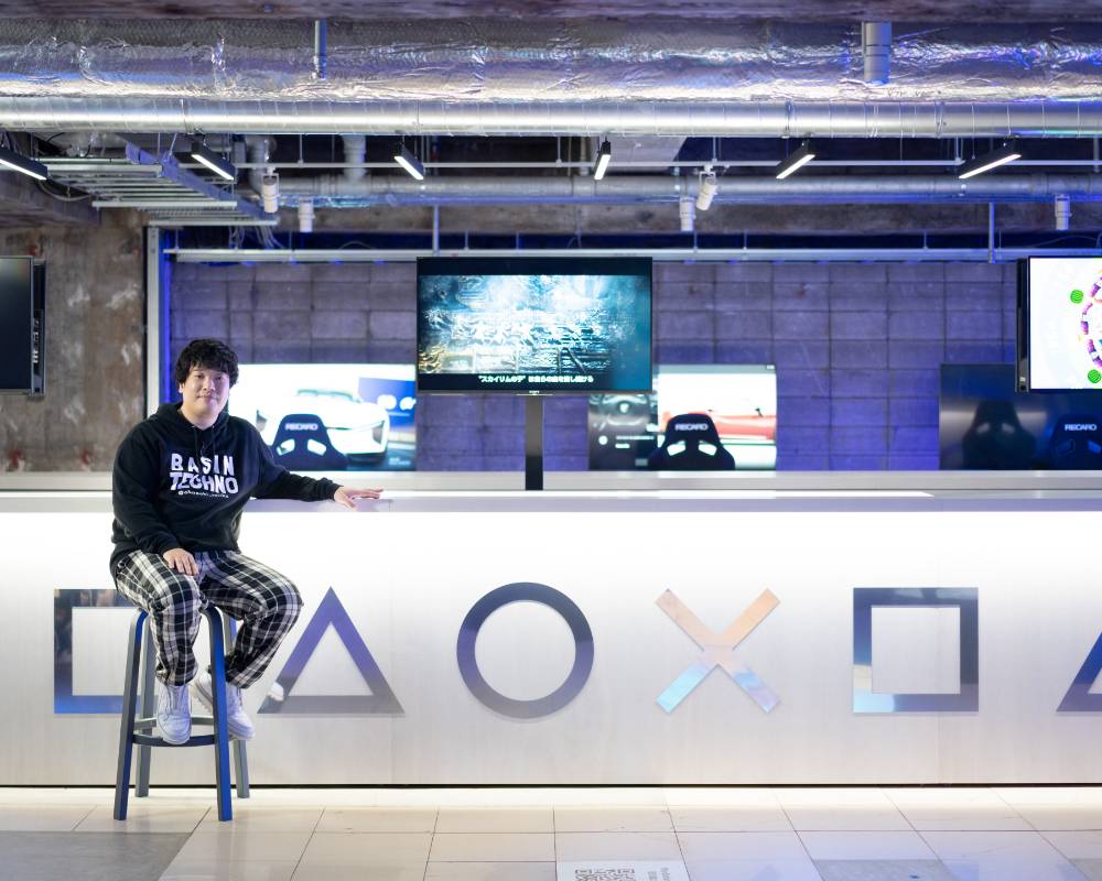 展示の様子。四角・三角・丸・バツのマークが描かれた大きなカウンターの手前にある椅子に岡崎体育が座っている。