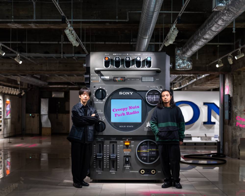 展示の様子。テレビ一体型ラジカセの巨大オブジェの前でCreepy Nutsの2人がポーズをとっている。