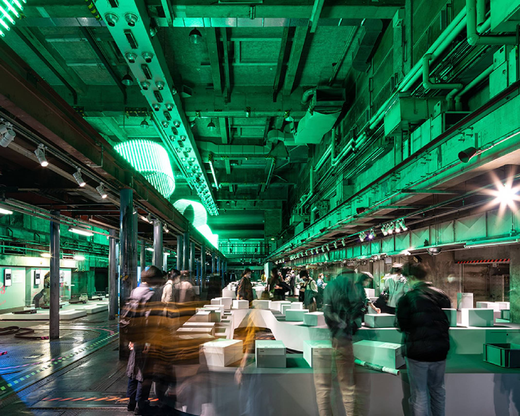 展示の様子。上層にある緑色に灯るオブジェの光が広がる地下空間の展示に人々が集まる。