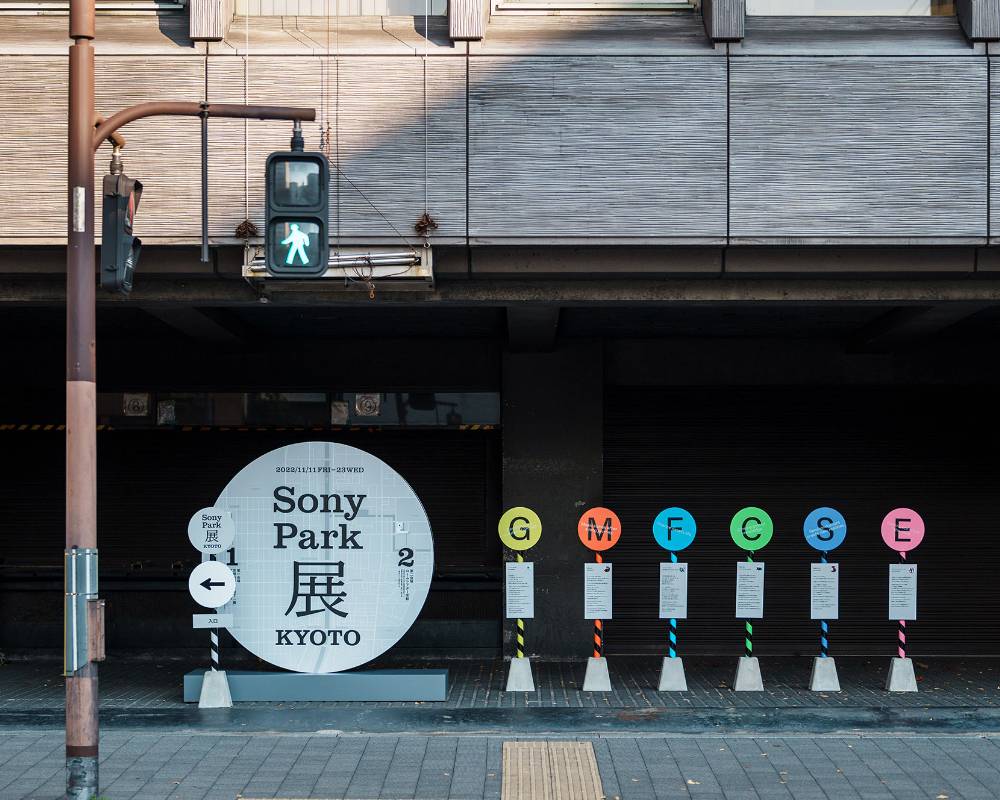 外観。屋外に、円形で表現されたメインビジュアルのサインと、6つのバス停のようなサインが並んでいる。