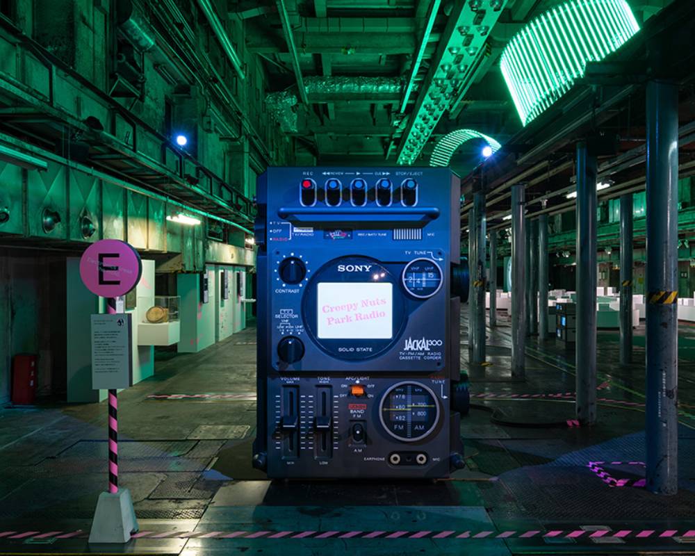 展示の様子。緑色の照明に彩られた空間にテレビ一体型ラジカセの巨大オブジェが展示されている。