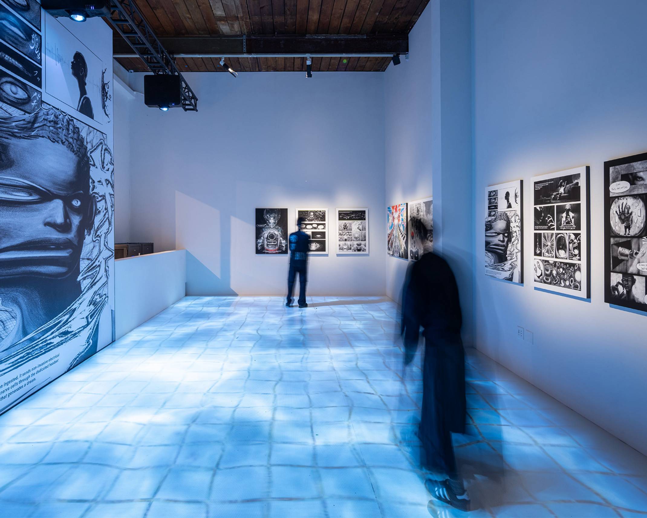 展示の様子。壁面にはマンガ『ドリームピル』のページが1枚ずつ展示され、床には水が張ったタイルのような映像が映し出されている。