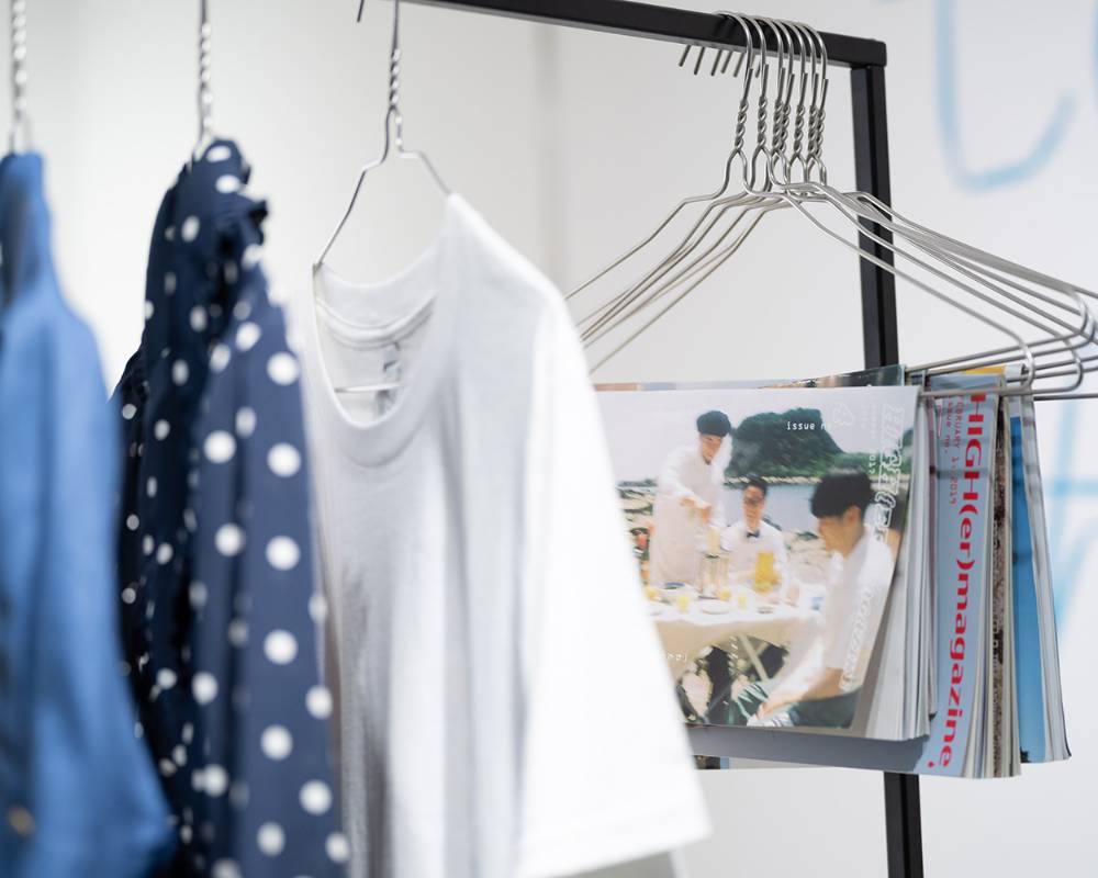展示の様子。ハンガーラックにはハンガーに掛けた洋服や雑誌が吊り下げられている。