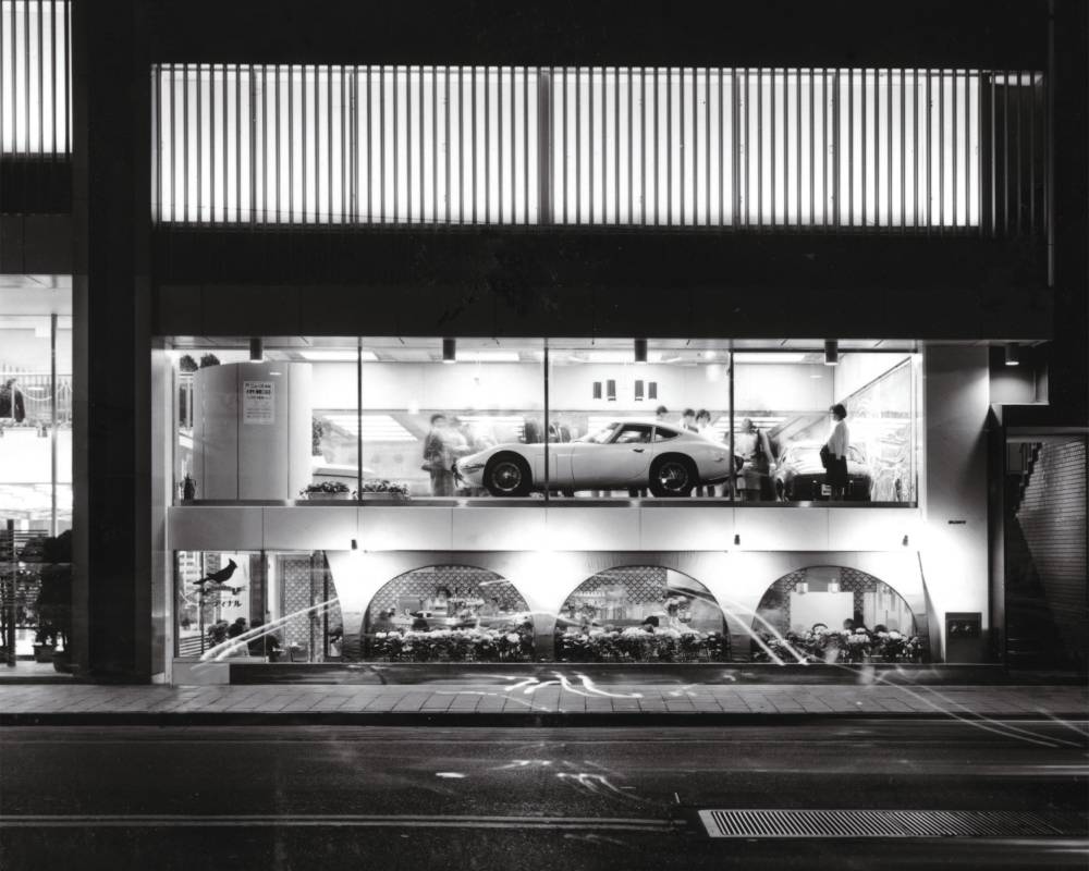 外観（モノトーン）。外堀通り側1階にはコーヒーショップがあり、2階にはウインドー沿いに車がディスプレイされている。