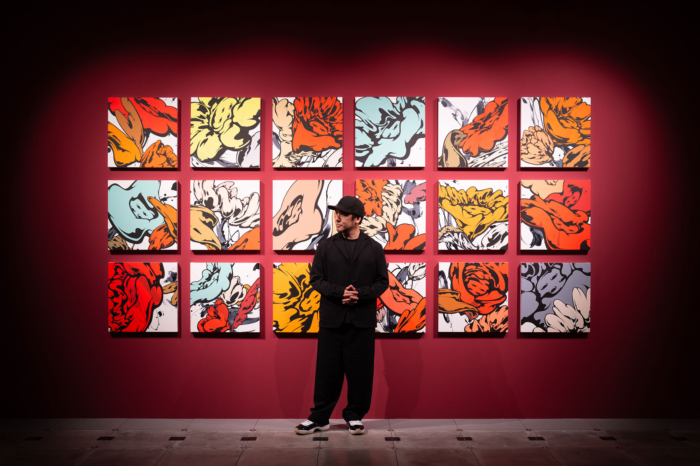 Exhibit. A person in black clothing is standing in front of various floral artworks displayed on a red wall.