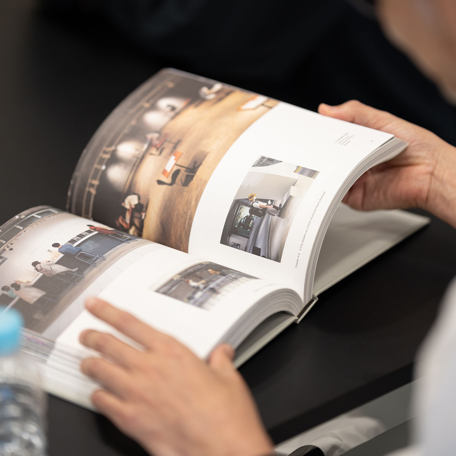 手前の人物が両手で書籍『Document of Ginza Sony Park Project』を開き、誌面をじっくりと見つめている様子。ページには、様々な角度から撮影されたSony Park内のアート展示や空間の写真が多数レイアウトされている。