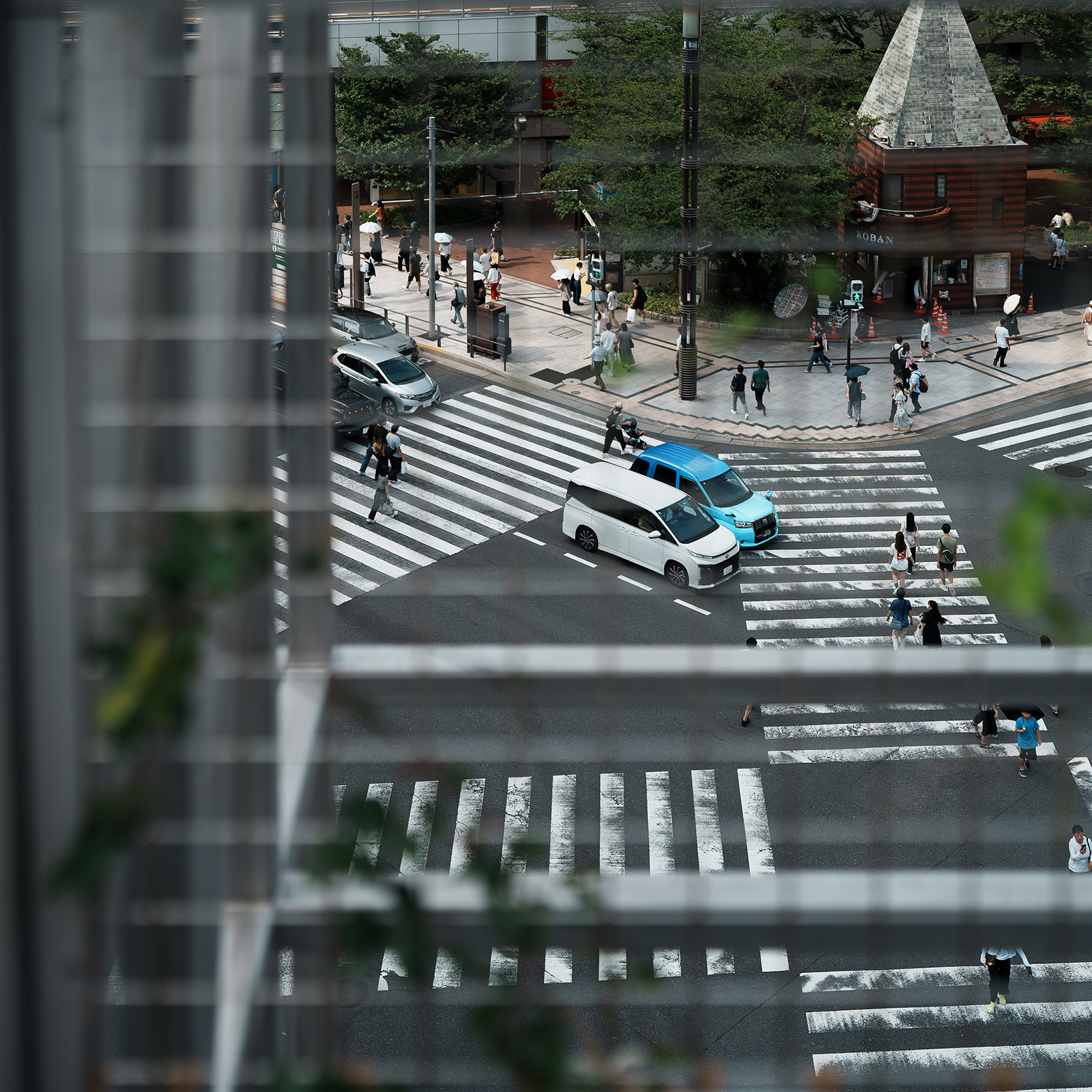 格子越しに見下ろす数寄屋橋交差点。白い車と人々が横断歩道を行き交う。