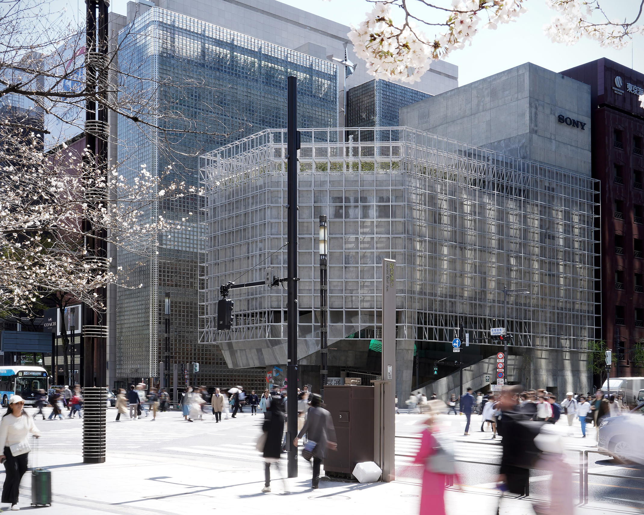 桜の花越しに見えるGinza Sony Parkの外観と、交差点を行き交う人々。