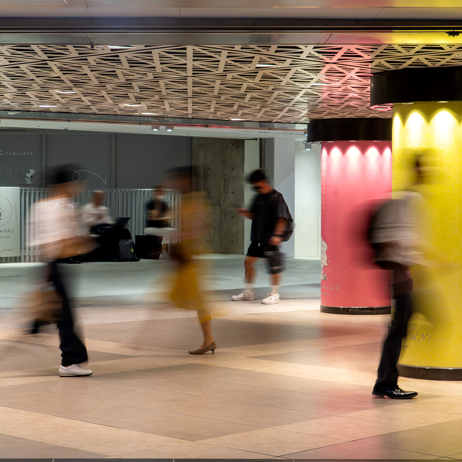 地下通路を歩く人々。天井の幾何学模様とピンクや黄色に彩られた柱が印象的。