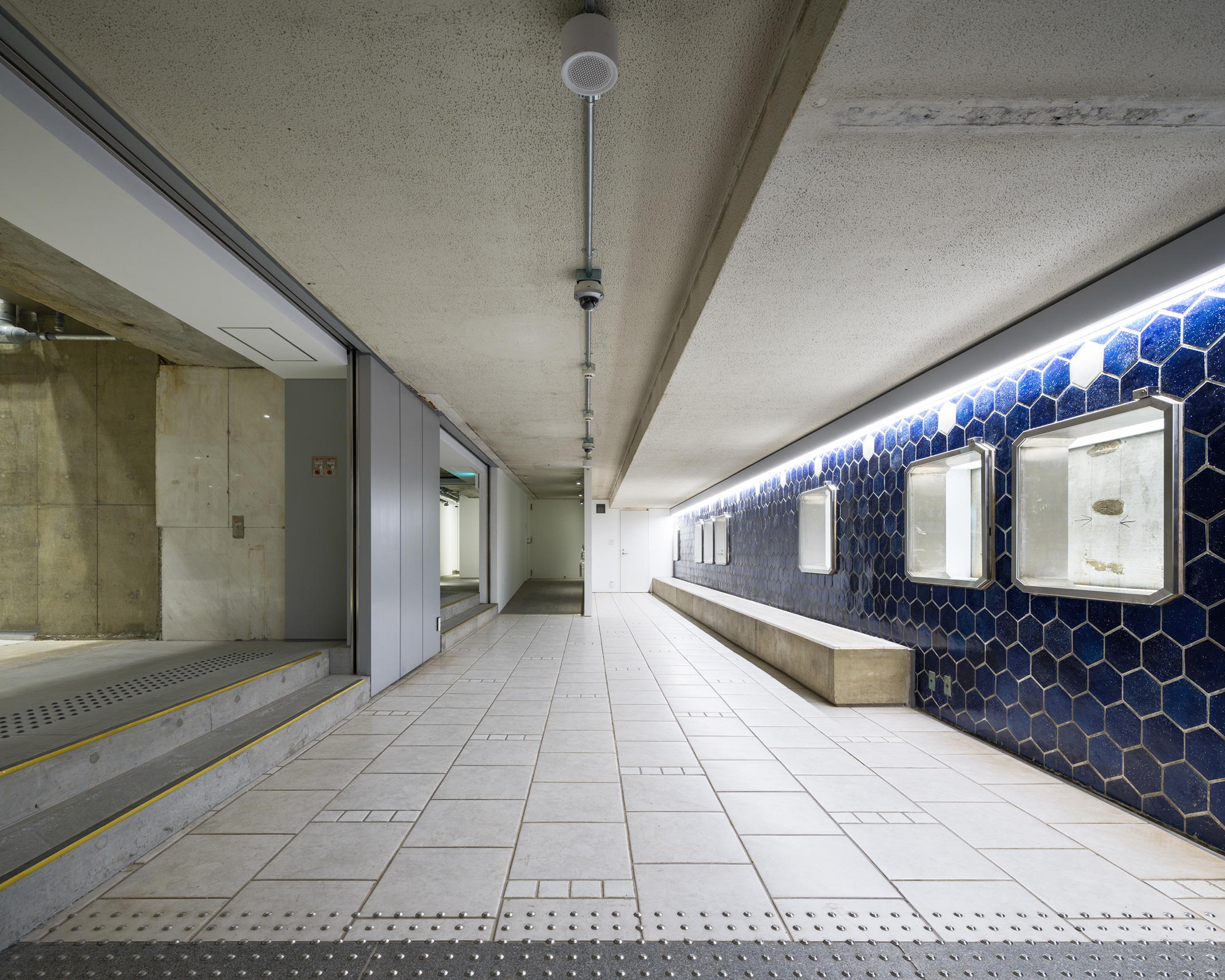 青い六角形タイルの壁が並ぶ地下の通路。壁には古いガラスケースが設置されている。