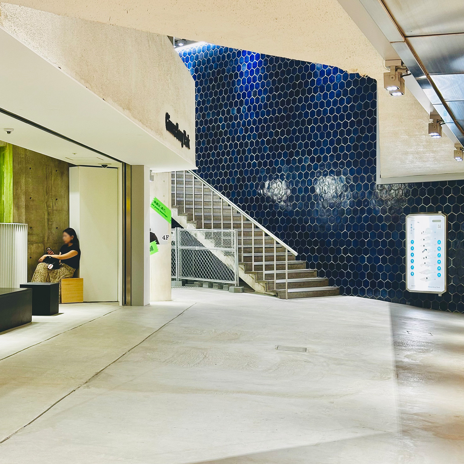 青い六角形タイルの壁と階段が目を引く地下フロア。ベンチに座る来園者の姿も見える。