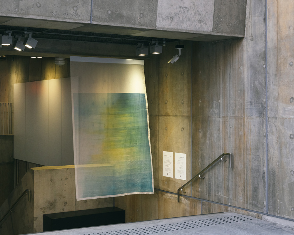Beside a stairway at Ginza Sony Park, a translucent fabric artwork hangs softly, its subtle colors contrasting with raw concrete walls.