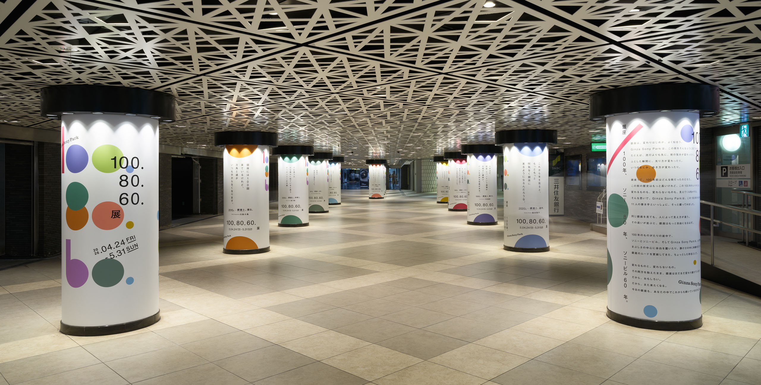 Ginza Sony ParkのB2を出た先、銀座駅コンコースに広がる柱展示。カラフルな円形グラフィックとテキストが柱を包み込み、幾何学的な天井と呼応しながら連続的な空間体験を生み出す。通行者の動線に沿って視覚的なリズムをつくる。