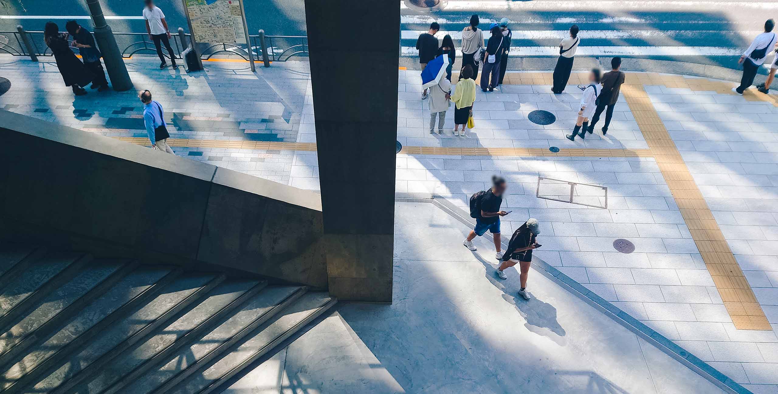 A stairwell at Ginza Sony Park. Pedestrians walk on the pavement above as sunlight and shadows intersect across the concrete surfaces.