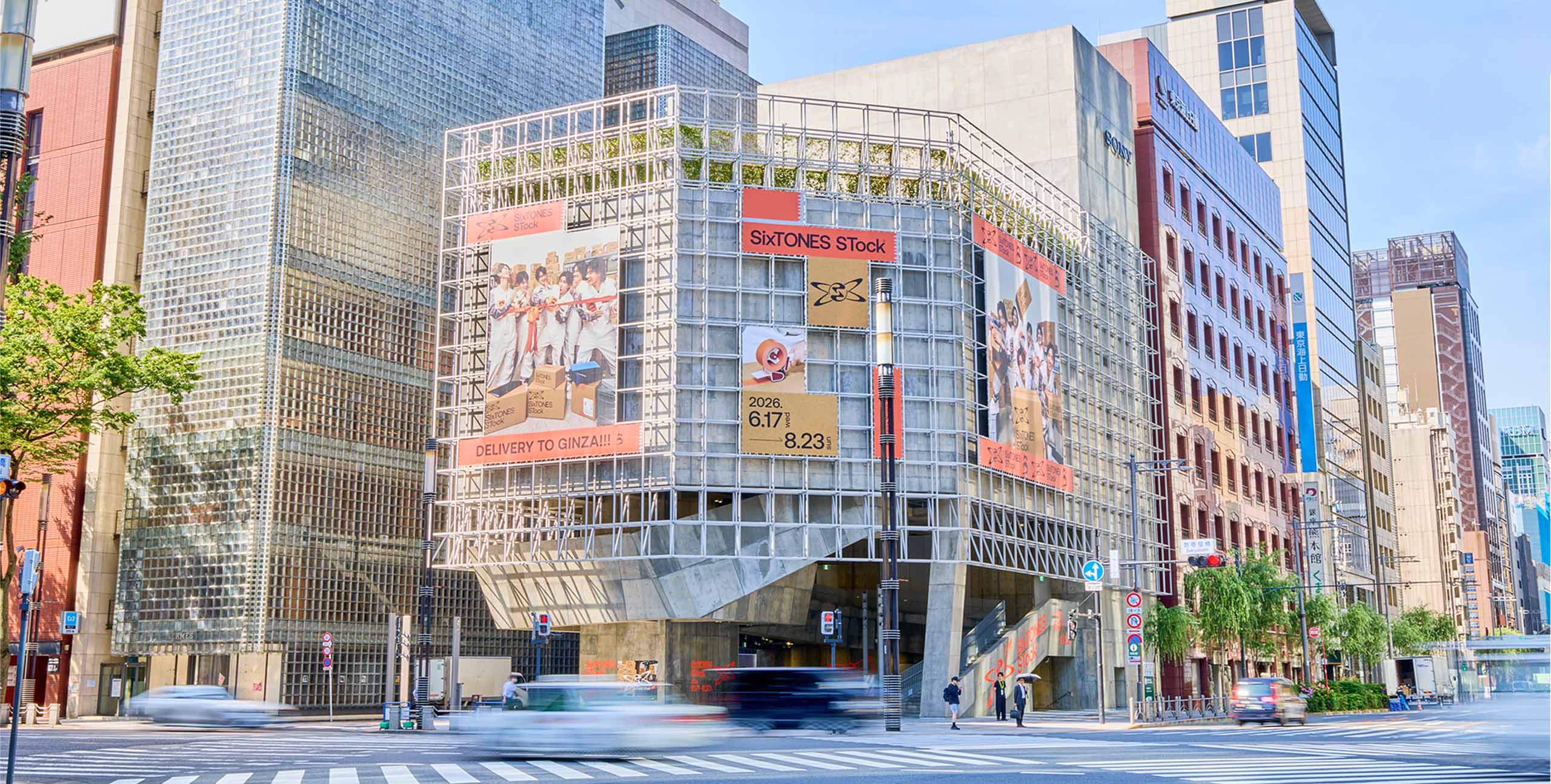 晴れた青空の下、銀座の交差点に建つGinza Sony Parkの外観。「SixTONES STock」の大型広告が掲示されたグリッドフレームがある建物。広告にはSixTONESのメンバーの写真や「2026 6.17-8.23」の日付が書かれている。